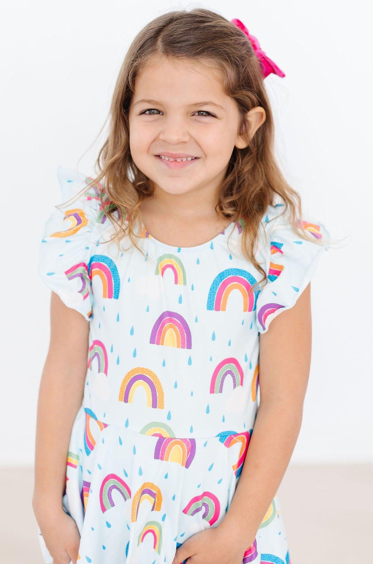 Little girl wearing April Showers Short Sleeve Twirl Leotard with rainbow raindrop pattern, smiling.
