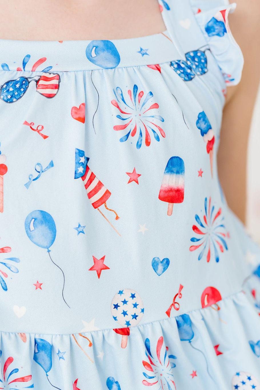 Light-blue dress with cross-back straps and ruffle shoulder, fireworks and balloons print.