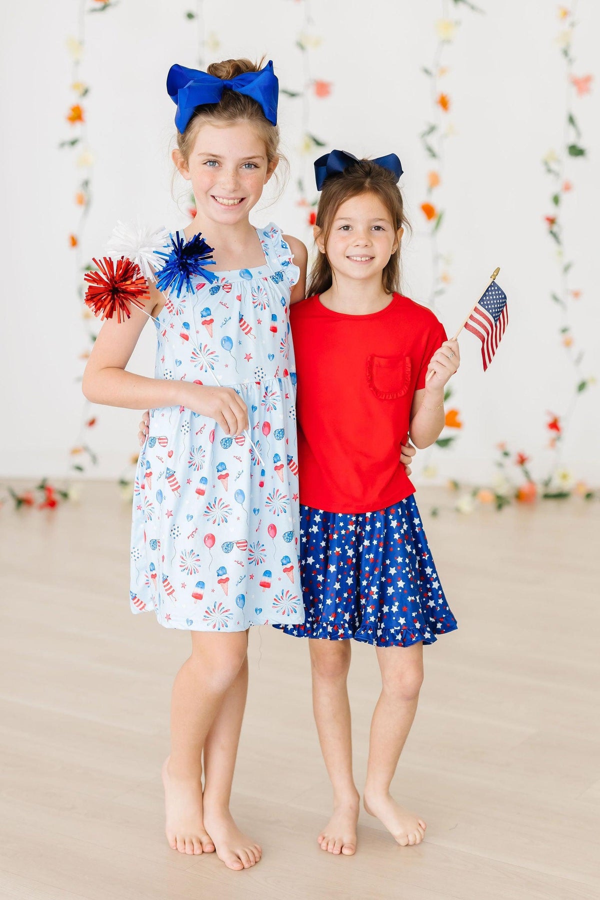 Two girls in patriotic outfits; Baby You're a Firework dress-inspired fireworks print with cross-back ruffle straps.