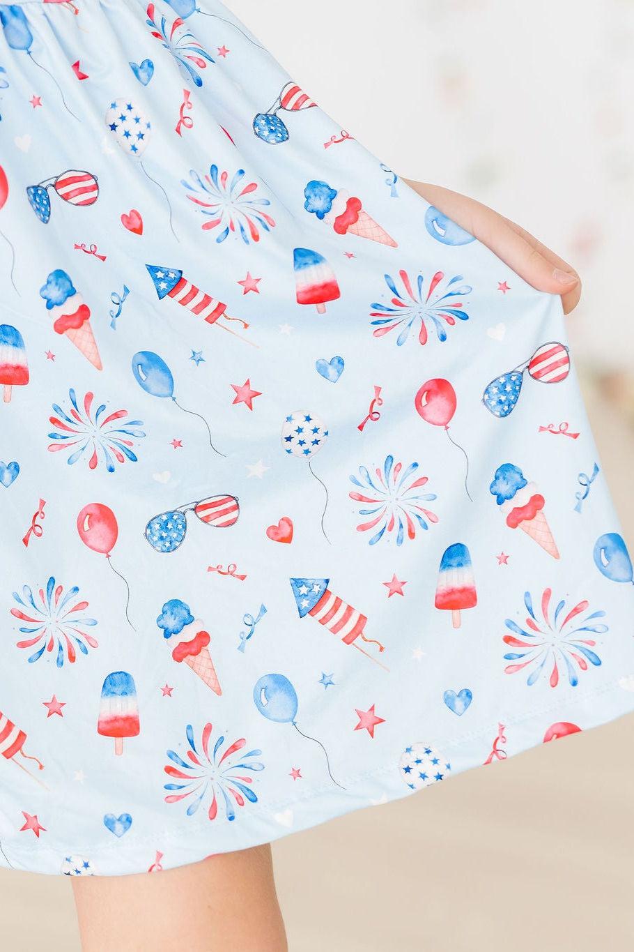 Baby You're a Firework Ruffle Cross Back Dress in light blue with patriotic fireworks print.