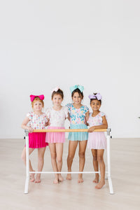 Four girls in pastel Ballerina Bows Short Sleeve Twirl Leotards pose at a ballet barre.
