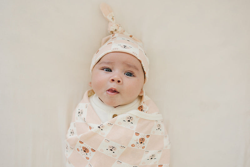 Baby wearing GOTS certified organic cotton knotted hat with checkered bear print, swaddled in matching blanket.