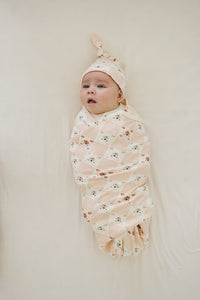 Baby wearing GOTS certified organic cotton knotted hat with checkered bear print, wrapped in matching swaddle.