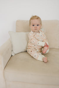 Baby sitting on beige sofa wearing GOTS certified organic cotton playsuit with checkered bear pattern and cream cuffs.