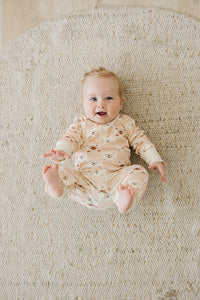 Smiling baby lying on woven rug wearing GOTS certified organic cotton playsuit featuring checkered bear print pattern.