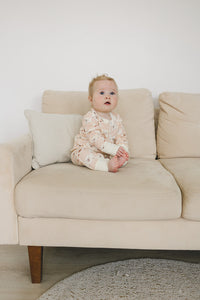 Baby wearing GOTS certified organic cotton playsuit with checkered bear print, sitting on beige sofa.