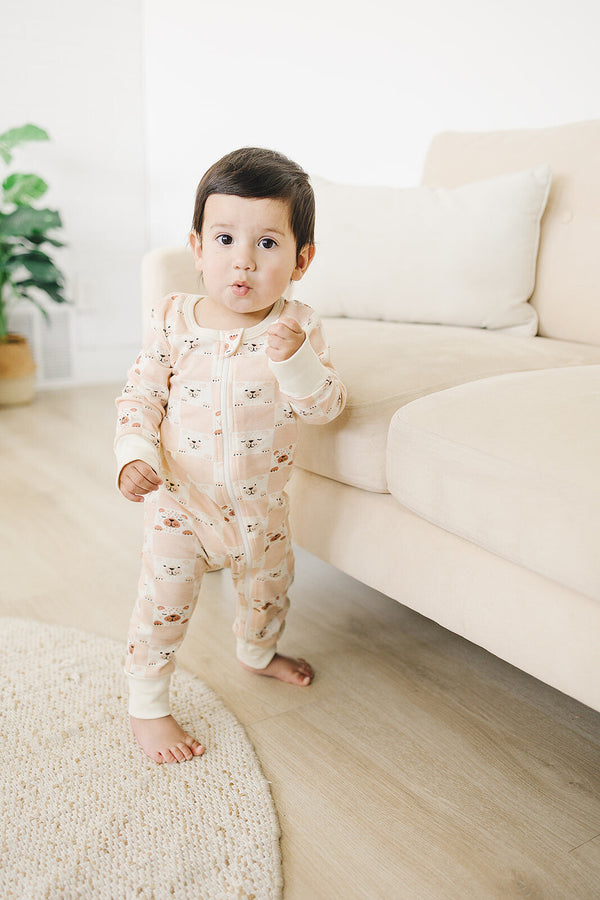 Baby standing in a GOTS certified organic cotton zippy romper featuring a pink checkered bear print and front zipper.