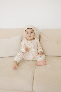 Baby wearing GOTS certified organic cotton zippy romper with checkered bear print and matching hat, sitting on beige sofa.