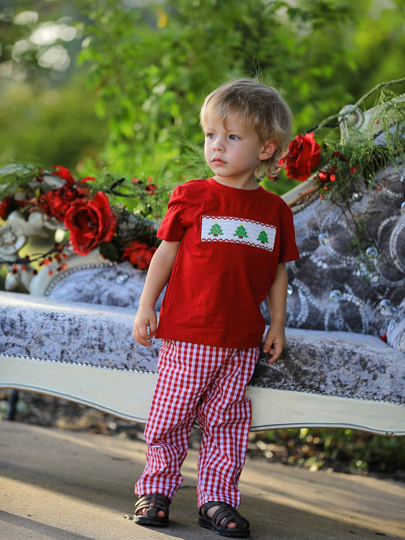 Toddler in red plaid outfit and brown sandals posing beside grey sofa with holiday decor