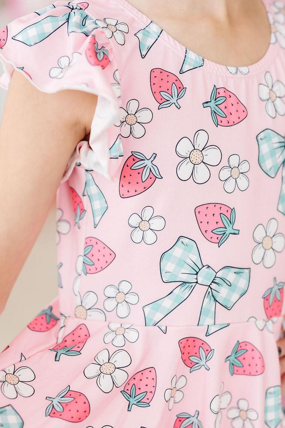 Berry Picnic Short Sleeve Twirl Leotard in pink with strawberry and daisy print and blue gingham bows.
