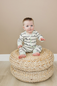 Baby wearing GOTS certified organic cotton zippy romper with toile print and mint trim, sitting on woven ottoman.