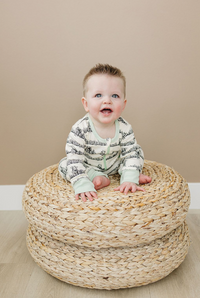 Happy baby sitting on a woven ottoman wearing a GOTS certified organic cotton zip romper with black print and mint green cuffs.