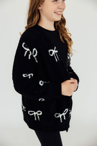 Cozy black cardigan featuring white bow patterns, styled over a black top and leggings for a soft, casual look.