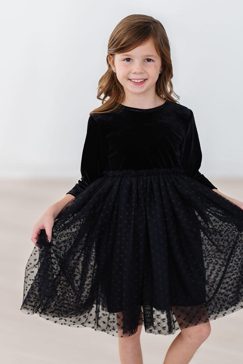 Girl wearing a Black Velvet Tutu Dress from Mila & Rose, showcasing its elegant design with a graceful scoop back and full tulle skirt, perfect for special occasions.