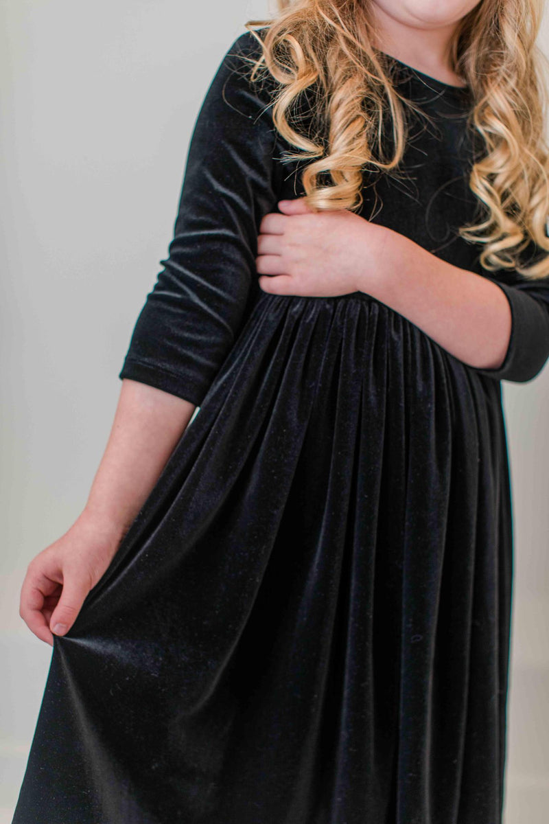 A young girl excitedly showcasing the SALE Black Velvet Twirl Dress from Mila & Rose®, featuring a flared skirt and elegant design, perfect for twirling and special occasions.