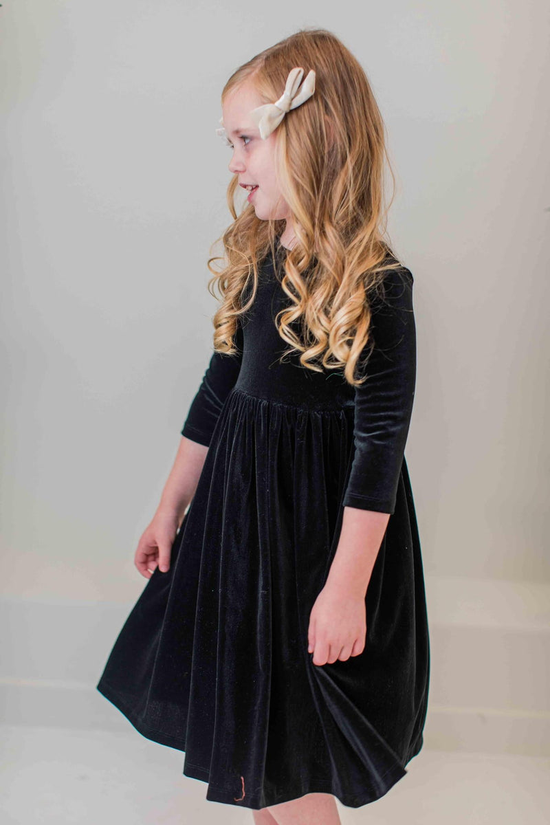 Side view of a girl wearing the SALE Black Velvet Twirl Dress from Mila & Rose®, highlighting the luxurious velvet fabric and classic silhouette, ideal for playful and elegant moments.