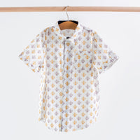 White short sleeve collared shirt featuring a repeating gold and purple fleur-de-lis print, with button front and chest pocket.