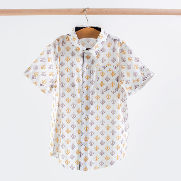 White short sleeve collared shirt featuring a repeating gold and purple fleur-de-lis print, with button front and chest pocket.