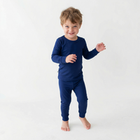 Smiling toddler boy wearing snug navy blue bamboo pajamas standing barefoot