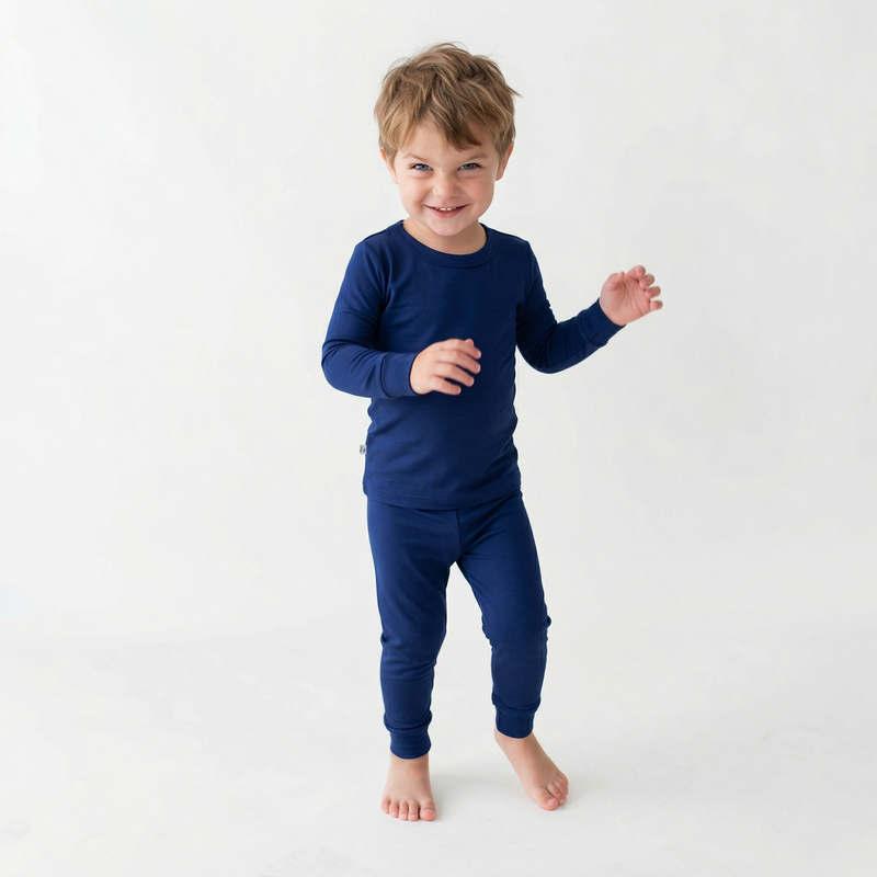 Smiling toddler boy wearing snug navy blue bamboo pajamas standing barefoot