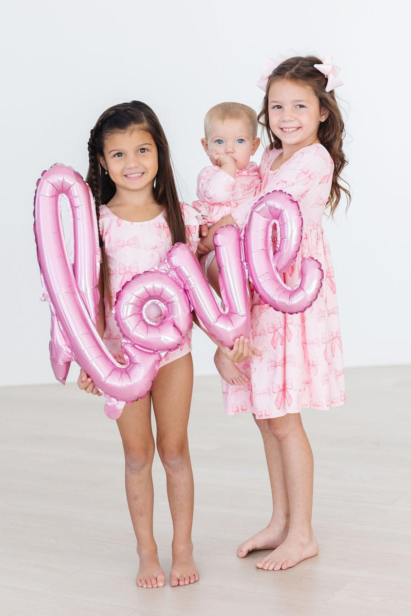 Adorable Blushing Bows 3/4 Sleeve Twirl Bodysuit from Mila & Rose, showcasing its stylish design in a playful setting.