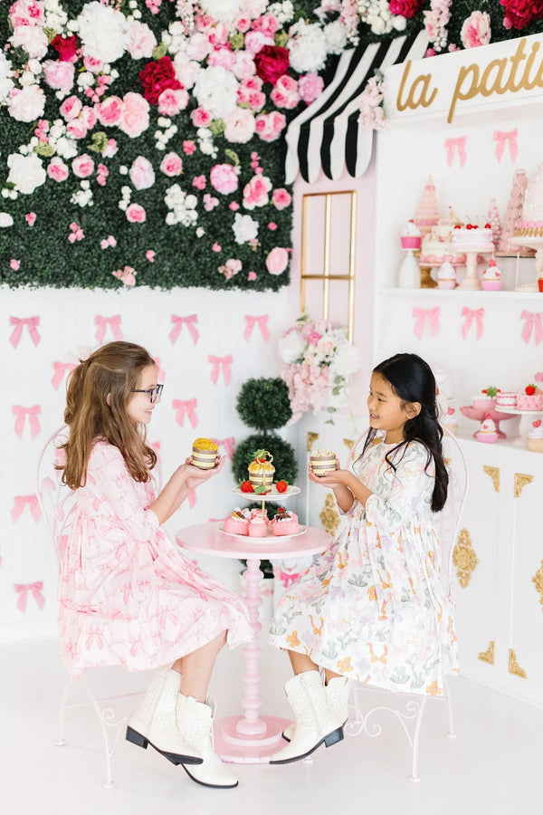 Girls wearing Mila and Rose boho bows twirl dress for girls in pastel pink and white sitting at a tea party