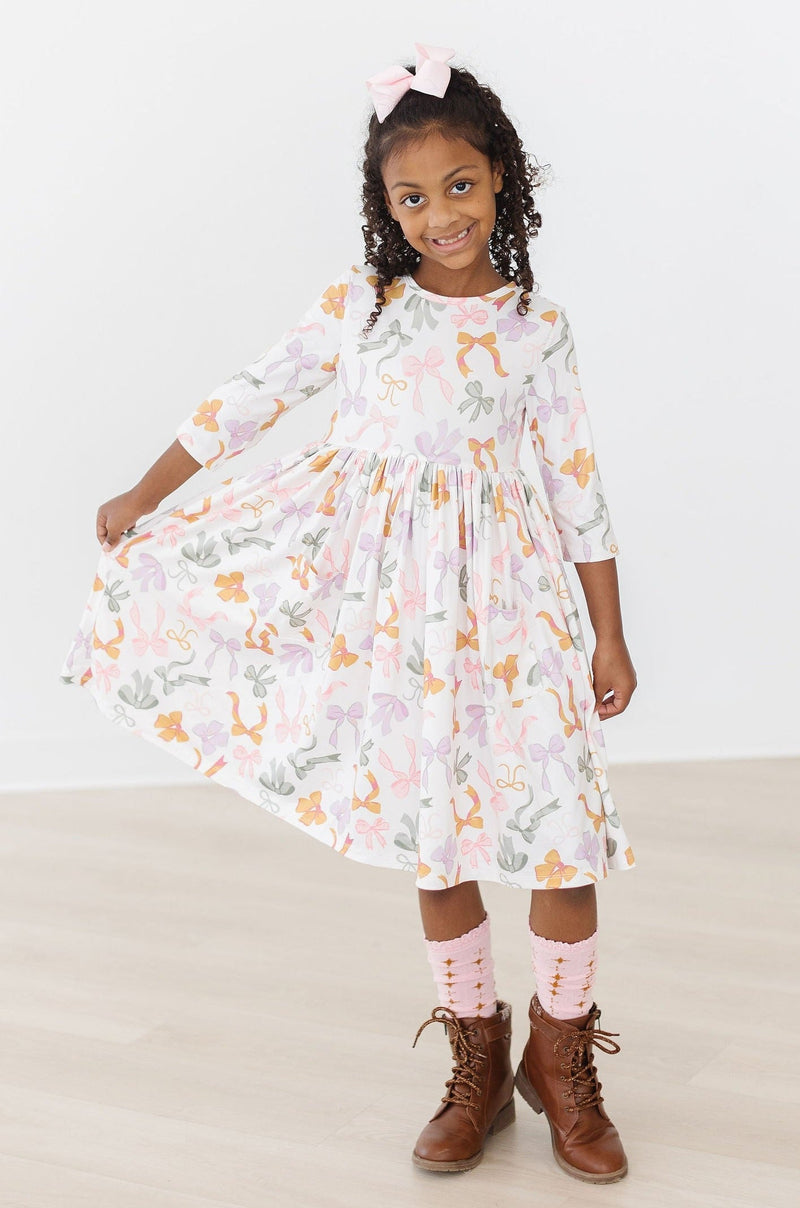 Boho Bows 3/4 Sleeve Pocket Twirl Dress hanging on a display, presenting its stylish scoop back closure and modest neckline.
