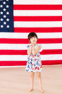 Born to Sparkle Flutter Sleeve Twirl Dress worn by a happy girl in front of a large American flag backdrop.
