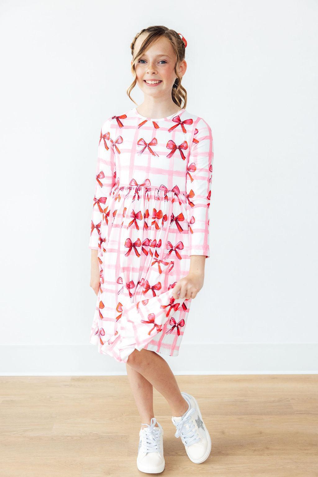 Bow La La Long Sleeve Pocket Twirl Dress on a smiling girl with pink bow print and twirl skirt.