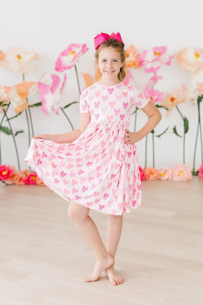 Young child wearing Bow Beauty S/S Pocket Twirl Dress by Mila & Rose ® while playing outdoors, demonstrating its versatility for everyday adventures.