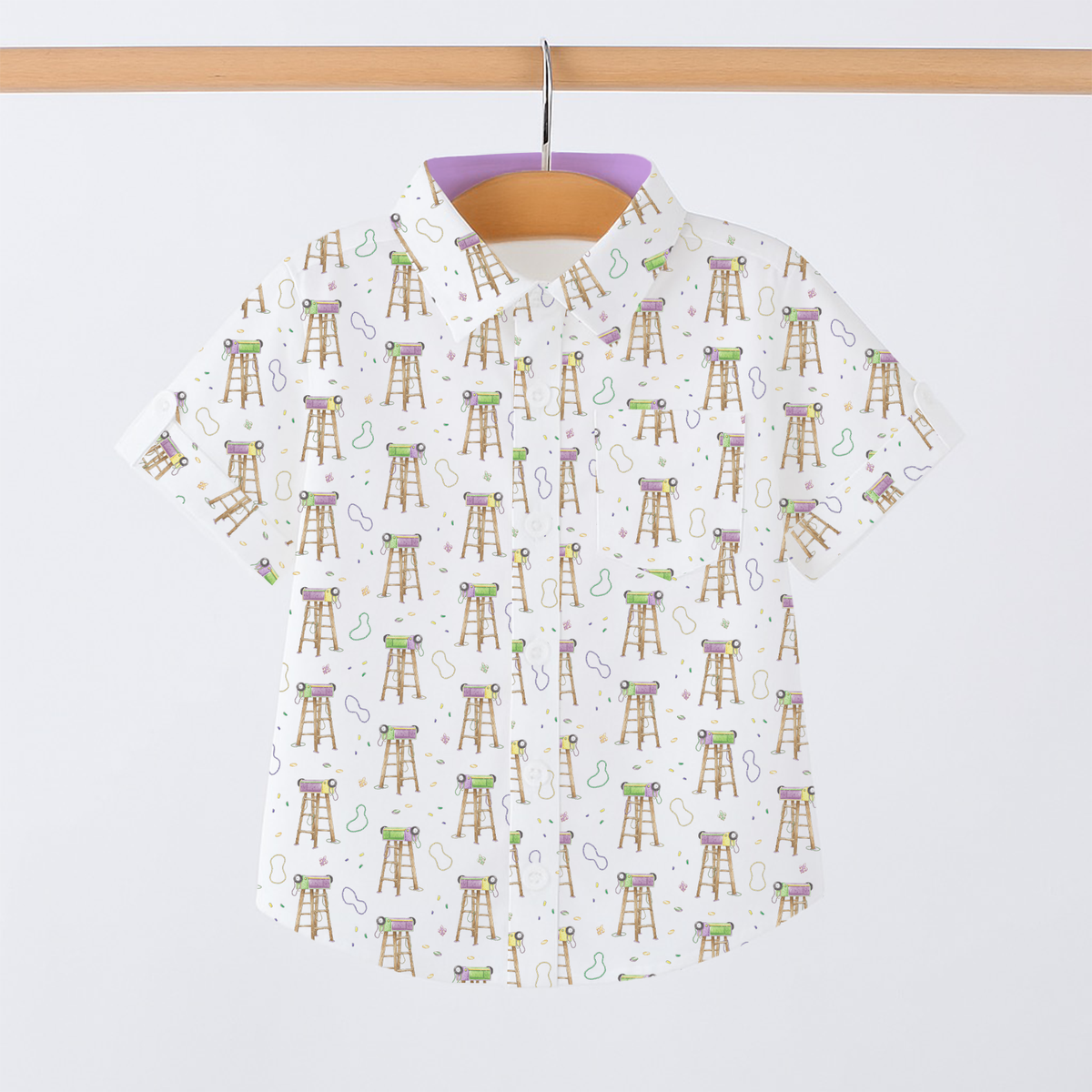 White short-sleeve collared shirt for kids with Mardi Gras ladder and bead print, hung on a wooden rod.