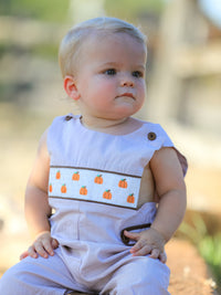 Baby boy in a blue pumpkin-embroidered smocked romper outdoors, fall-themed.