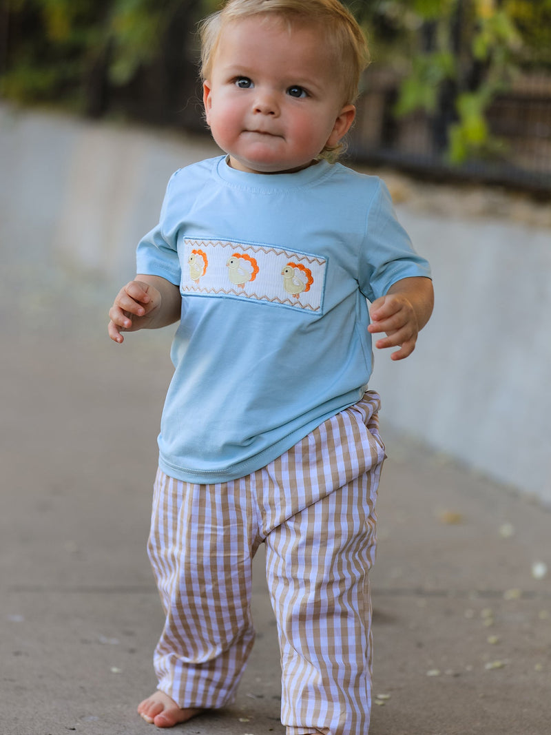 Toddler boy in light blue shirt with three orange yellow chick embroidery and tan white gingham plaid pants walking outdoors
