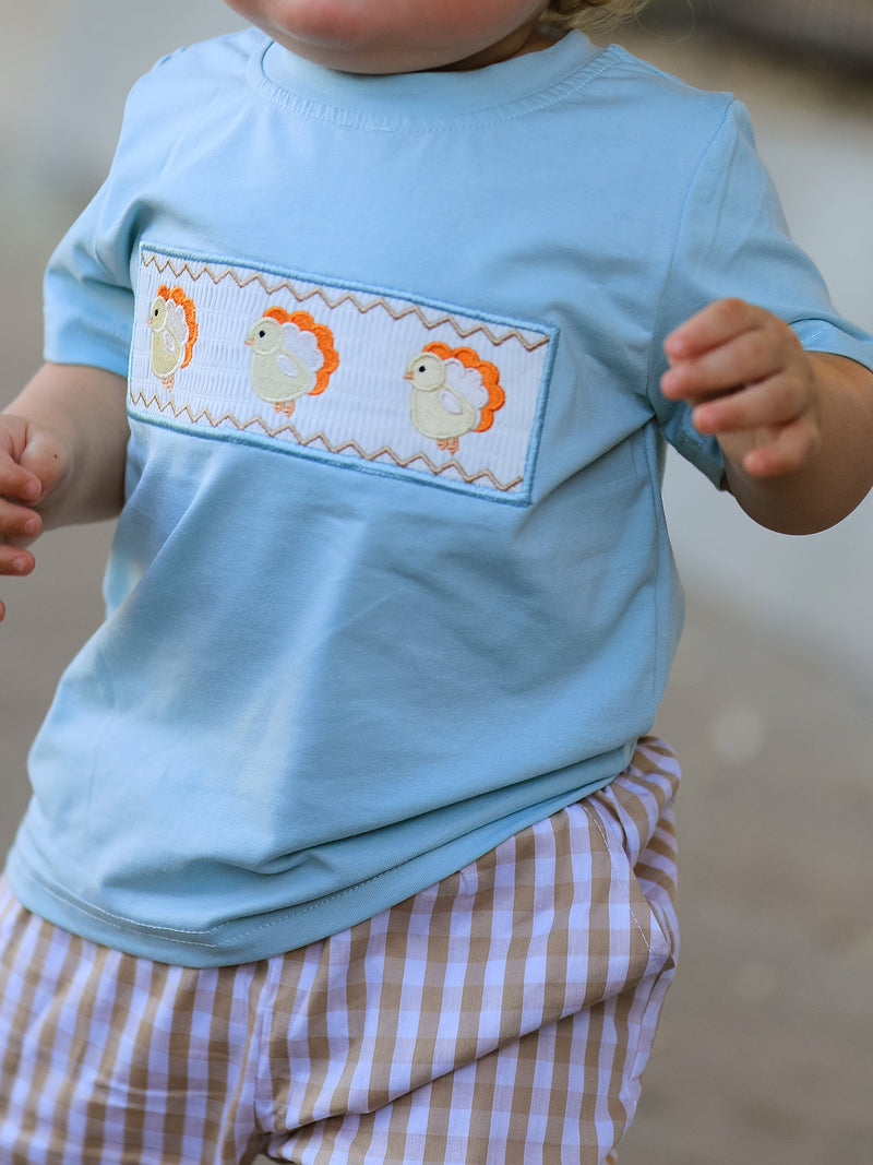 Close up of light blue t shirt chest showing white smocked panel with three stylized chick appliqués and zigzag stitching