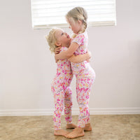 Two children embrace in The Second-Skin 2-Piece Short Sleeve Pajama in pink butterfly-print.