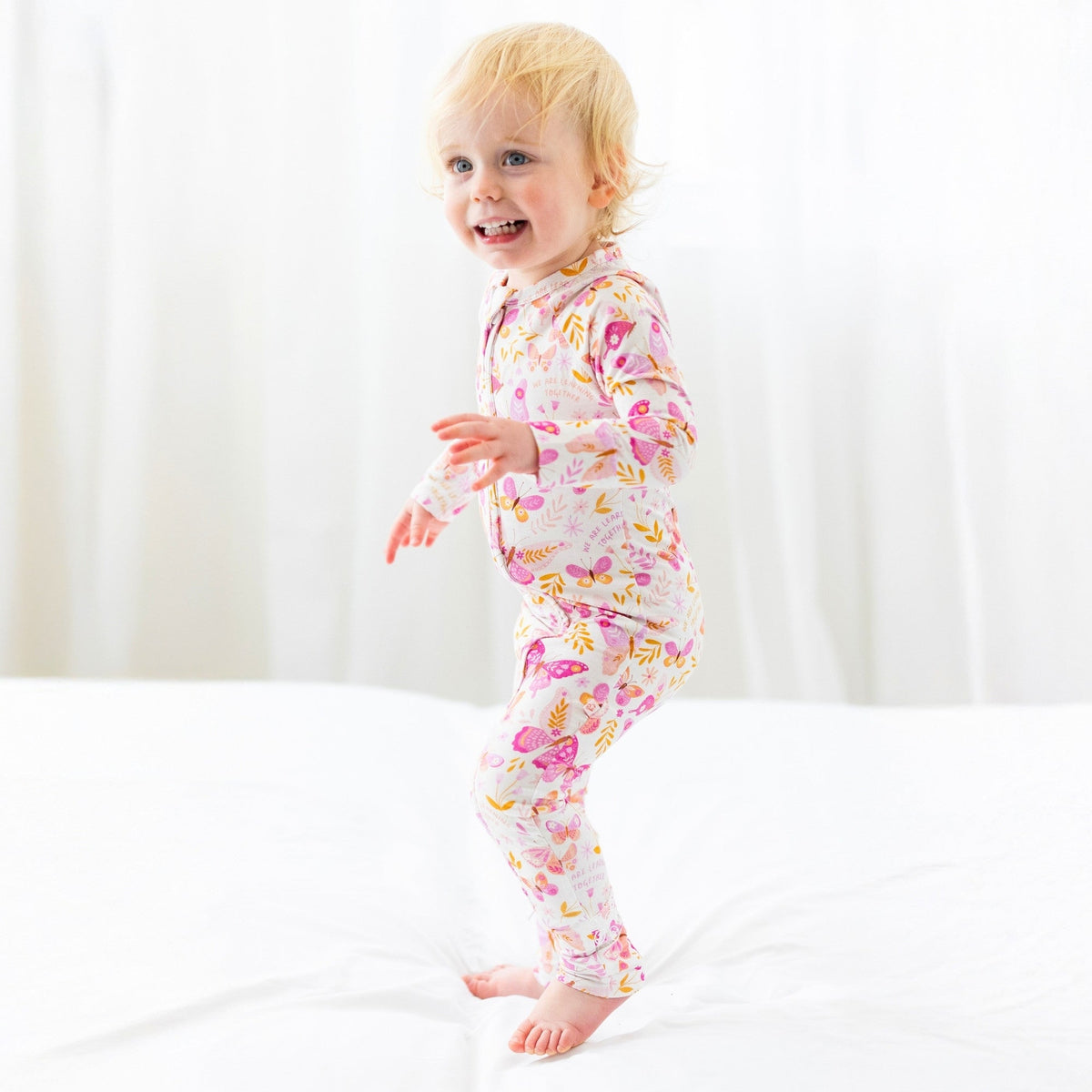 Child wearing Second-Skin Convertible Romper in pink butterfly print with front zip, Raising Mama viscose fabric.