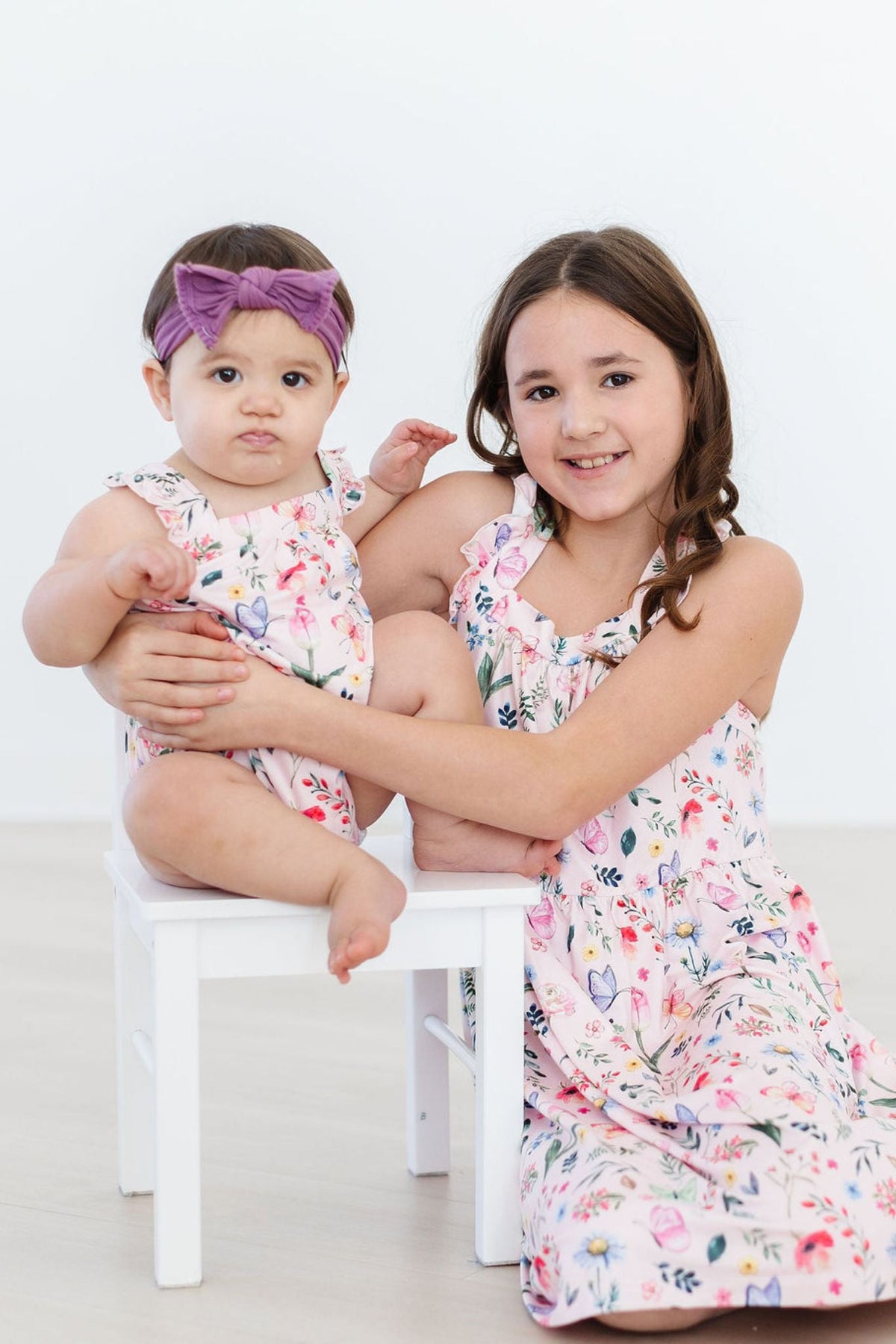 Two sisters in matching Butterfly Meadows Ruffle Cross Back Dress and baby romper.