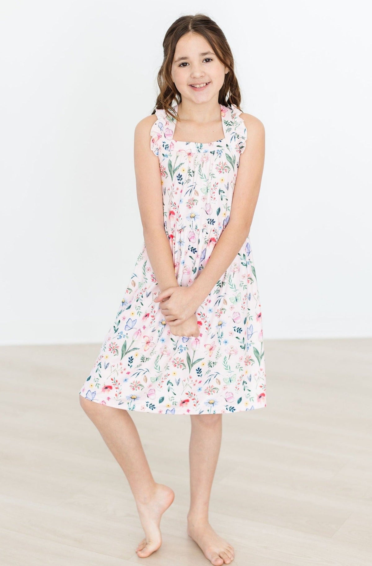 Girl in a floral Butterfly Meadows Ruffle Cross Back Dress with crisscross back straps and ruffled shoulders.