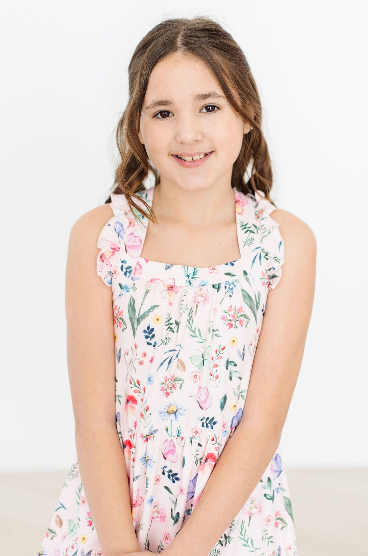 Butterfly Meadows Ruffle Cross Back Dress worn by a smiling girl in a pastel floral sundress.