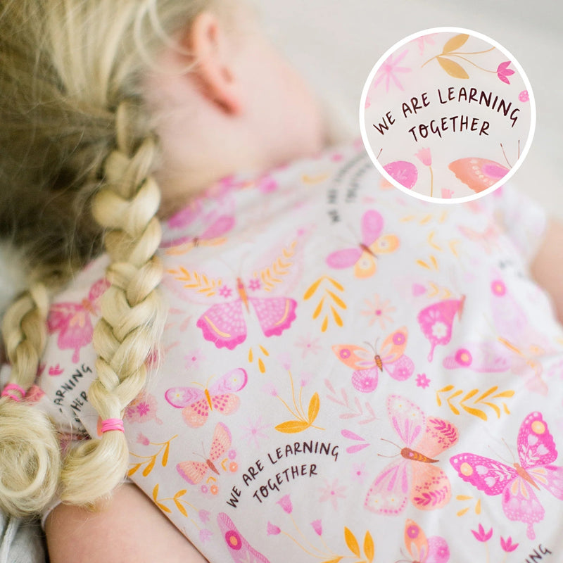 Person wearing pink floral second-skin two-piece pajama set with circular badge reading We Are Learning Together.