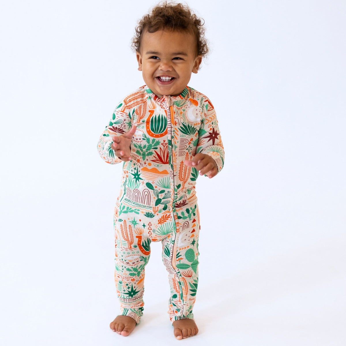 Smiling toddler in Desert Cactus beige convertible zippered romper with cactus-leaf print on Raising Mama viscose.