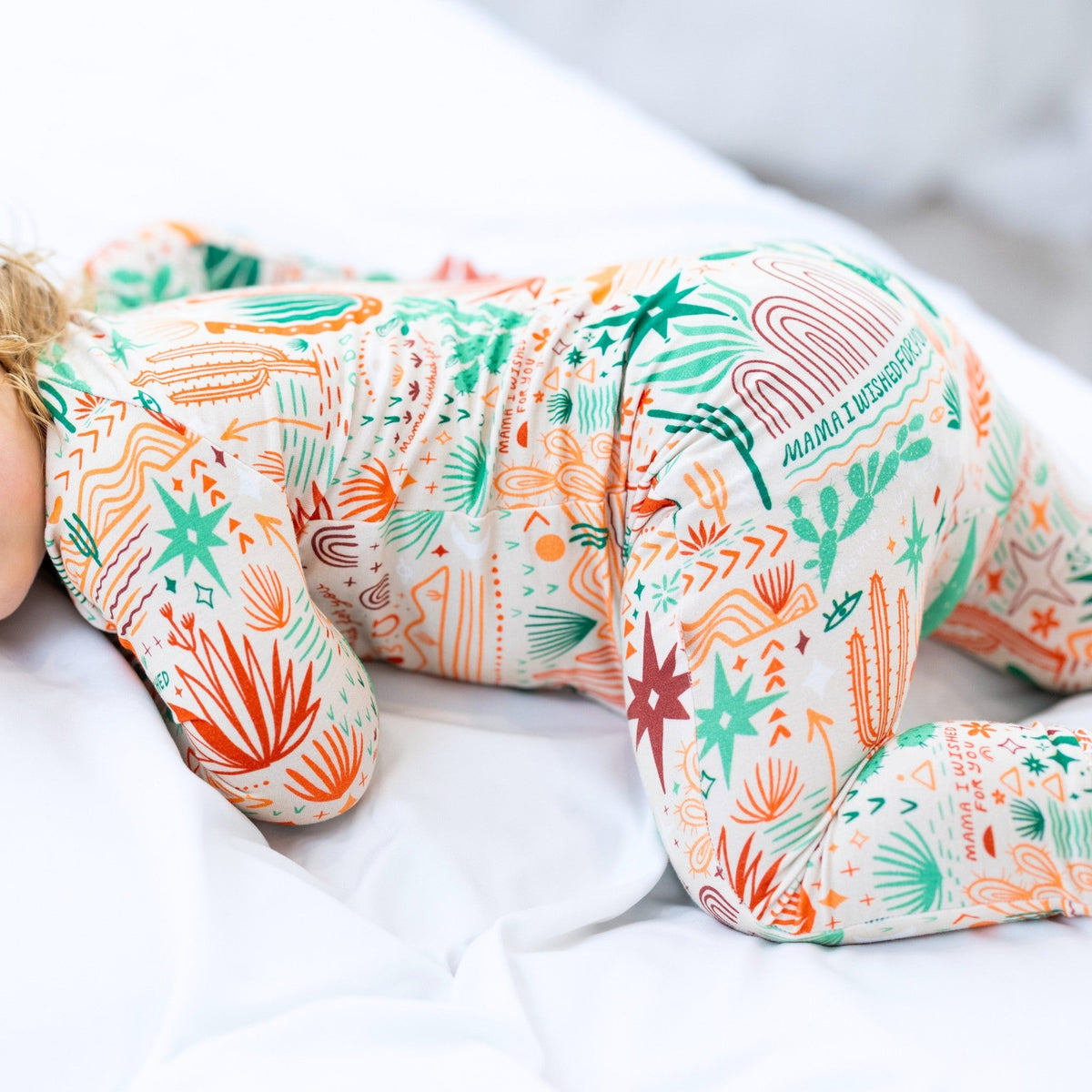 Desert Cactus beige Second-Skin Convertible Romper, close-up of teal and orange cactus print on white bedding.