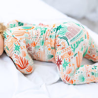 Desert Cactus beige Second-Skin Convertible Romper, close-up of teal and orange cactus print on white bedding.