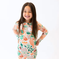 Happy child in beige Desert Cactus two-piece long-sleeve pajama set with cactus print.