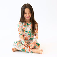 Smiling girl wearing Desert Cactus beige two-piece long-sleeve pajama with cactus print.