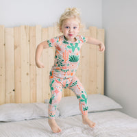 Child wearing Desert Cactus beige two-piece short-sleeve pajama, jumping on bed.