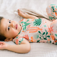 Baby in beige Desert Cactus print pajama set, lying on a bed.