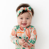 Baby wearing The SoftKnot Bow Desert Cactus (Beige) bamboo head-wrap, cozy and soft.