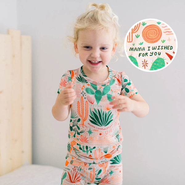 Smiling toddler in beige Desert Cactus 2-piece short-sleeve pajama set with cactus print.