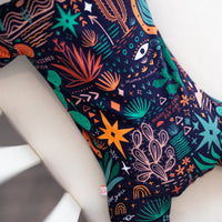 The Second-Skin Footie in Desert Cactus Midnight, a navy baby zippered onesie with colorful hand-drawn desert motifs.